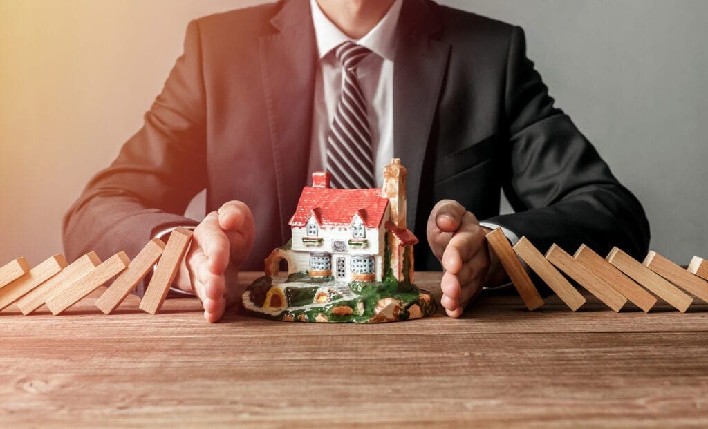 Close-up of a man stopping the wooden blocks from falling on house model. House insurance and security concept. Close-up of a man stopping the wooden blocks from falling on house model. House insurance and security concept.