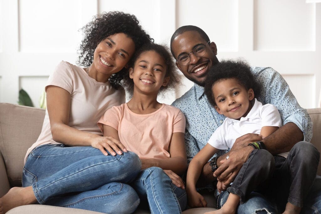 Portrait of black family with kids relax on couch Portrait of happy young african American family with little kids sit relax on couch cuddling, smiling black parents rest on sofa hug preschooler children posing for picture at home together
